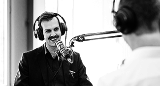 Ein Mann sitz mit seinen Kopfhörer vor einem Mikrofon und wird für einen Podcast aufgenommen.