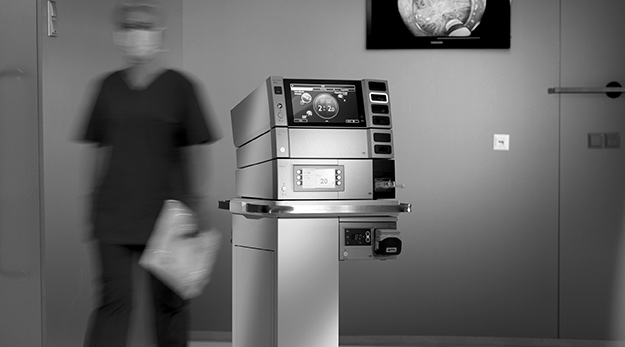 VIO 3n Elektrochirurgie-Workstation in einem Operationssaal, im Hintergrund geht eine unscharf abgebildete medizinische Fachkraft vorbei.